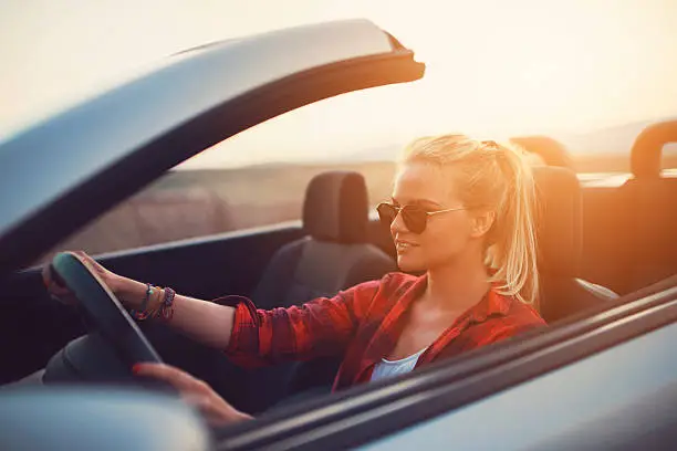 Beautiful young woman with sunglasses driving a cabrio.