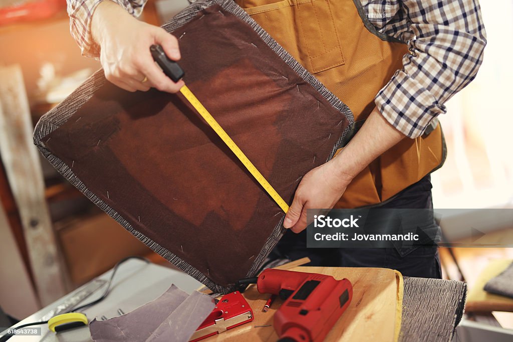 Hombre tapicando silla en su taller, medir tabla de madera - Foto de stock de Tapicero libre de derechos