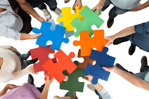 Directly above shot of people holding colorful puzzle pieces in huddle against white background