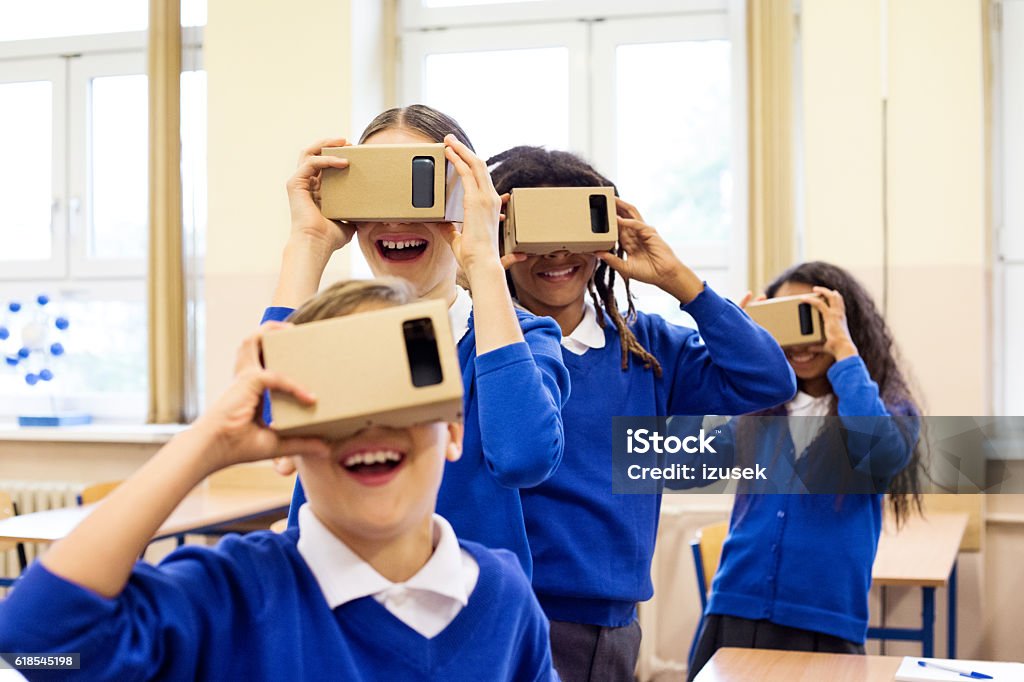 School kids using virtual reality goggles Multi ethnic group of students using virtual reality cardboard goggles in the classroom. Education Stock Photo