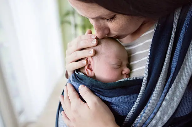 Photo of Close up, beautiful mother kissing her son in sling