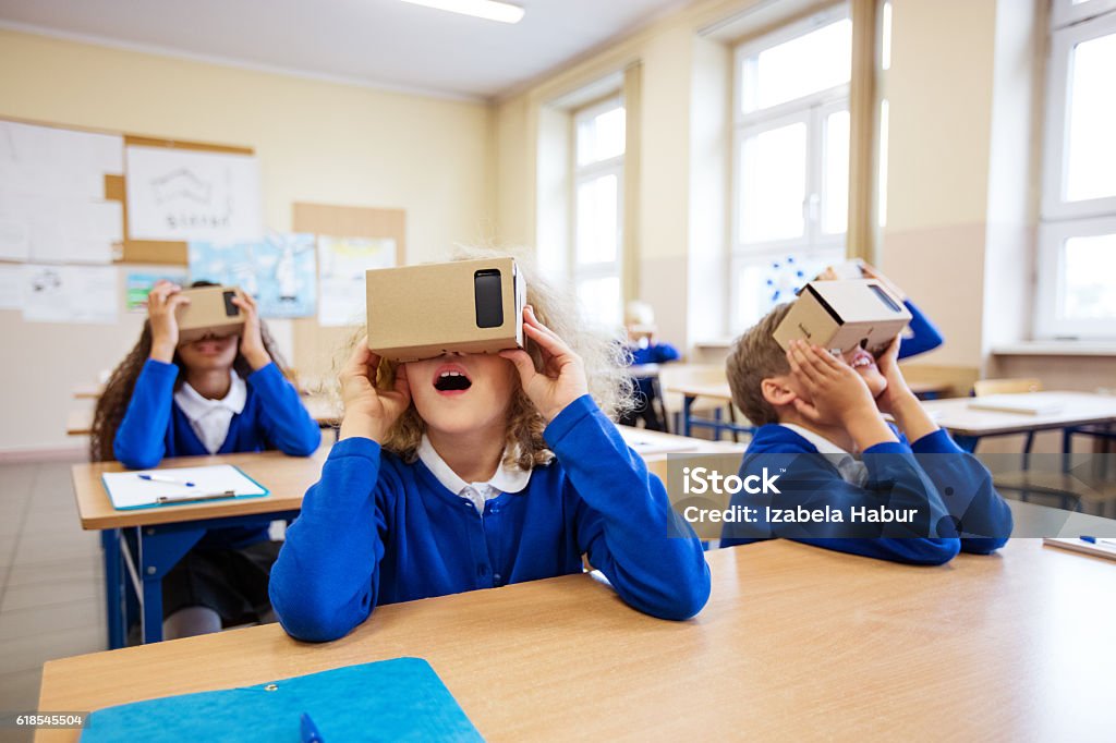 School kids using virtual reality goggles Multi ethnic group of students using virtual reality cardboard goggles in the classroom. School Uniform Stock Photo