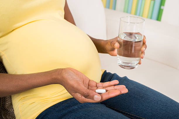 Pregnant Woman Taking Medicine At Home Close-up Of Pregnant Woman Hand With Glass Of Water And Vitamin Pill folic acid stock pictures, royalty-free photos & images