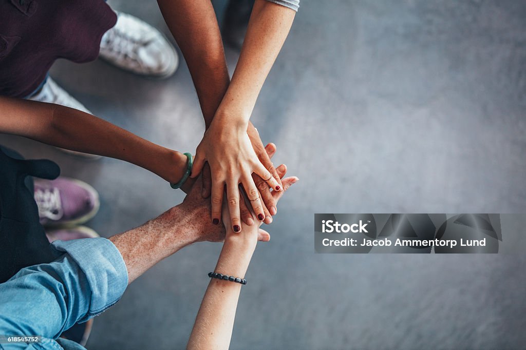 Group of young students showing unity Cropped image of young people's hands on top of each other. Top view of young group with hands on stack. Support Stock Photo