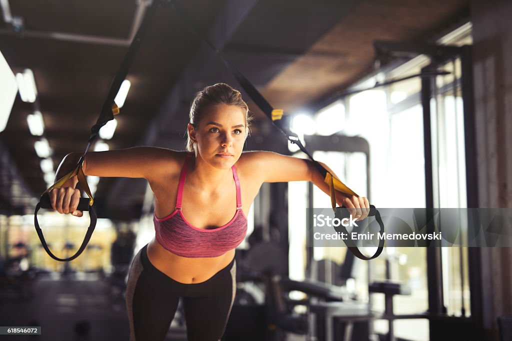 Woman doing arm exercises with suspension straps at gym. Young athletic woman having sports training and doing arm exercises with suspension straps exercises at gym. Exercising Stock Photo