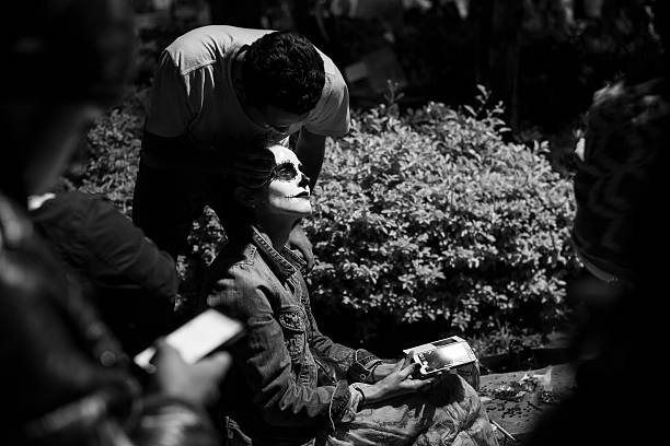 Oaxaca, Mexico - November 1, 2014: A woman from Colombia gets her face painted at night during Day of the Dead (Dia de los Muertos) festivities in Oaxaca, Mexico. A Samsung smartphone is in her hand.