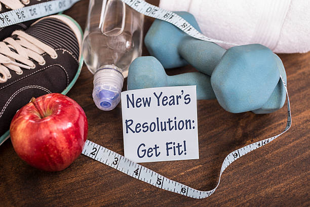 New Year's Resolution to get healthy. New Year's Resolution to get healthy in January of the coming year. Image features: dumbbells, sports shoes, water bottle, apple, towel, tape measure on wooden table. Adhesive note reading "New Year's Resolution: Get Fit!" in foreground. Fitness concept. 2019 new year resolution stock pictures, royalty-free photos & images