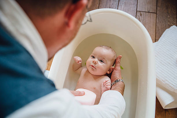Baby Bathtime Baby girl being washed in a bath by her father. She is looking at him. girls bath stock pictures, royalty-free photos & images