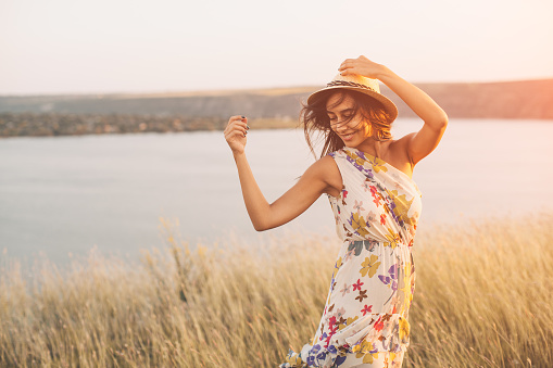 Beauty young girl outdoors enjoying nature. Fashion young woman in floral dress and stylish hat in meadow with copy space