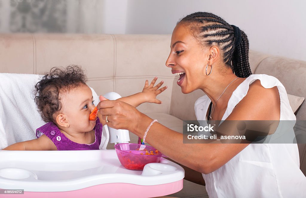 Mother Spoon Feeding Her Baby African-American Mother Feeding Baby Girl In High Chair Baby - Human Age Stock Photo