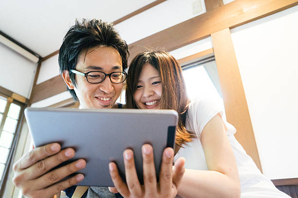 Cheerful Japanese friends using tablet indoors stock photo