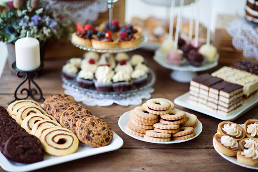 Brown wooden table with various cookies, tarts, cakes, cupcakes and cakepops. Studio shot.