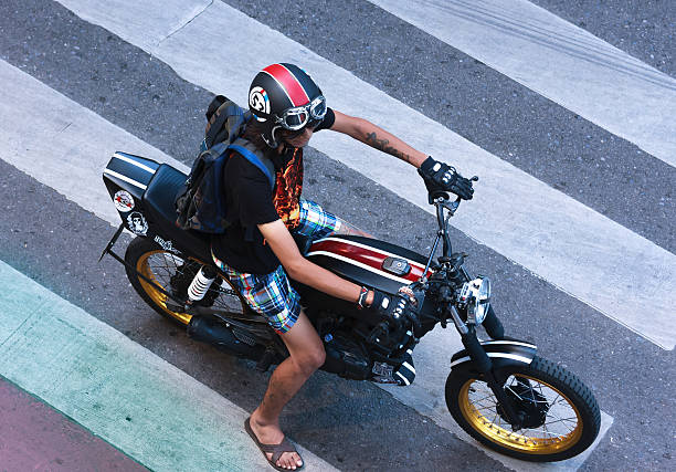 Bangkok, Thailand - June 19, 2015: Young man in casual clothing rides on a vintage motorbike stopped at the red light at Ratchaprasong Junction in the evening