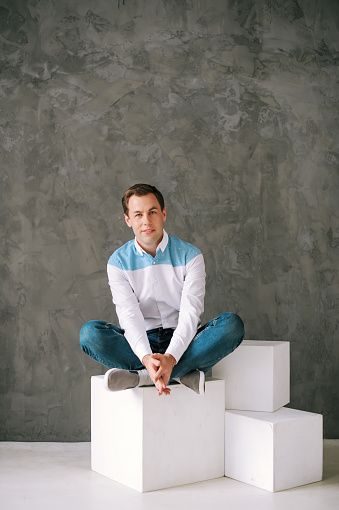 Happy man wearing casual clothes. The man sits on a white cube in studio.