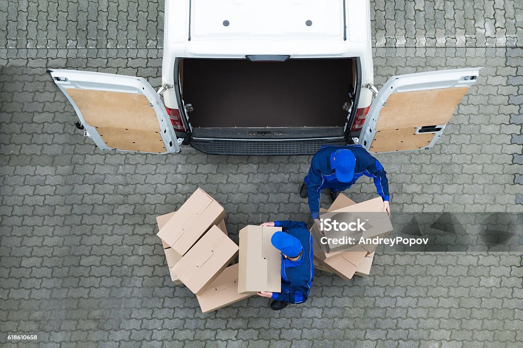 Delivery Men Unloading Cardboard Boxes From Truck On Street Directly above shot of delivery men unloading cardboard boxes from truck on street Delivery Van Stock Photo
