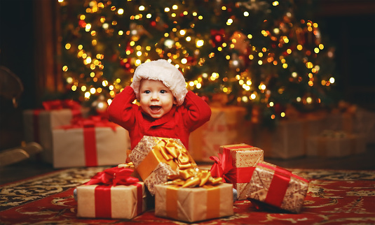 Happy baby by a Christmas tree with gifts
