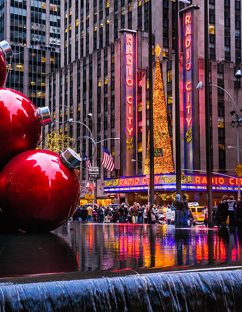  New York City, New York, USA  - December 27, 2012: Crowds of shoppers and tourists walk along the sidewalk outside Radio City as the Christmas lights are reflected in the outdoor fountain.