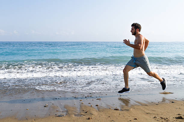 istock Man runner sprinting on wet sand run at the beach 618615356