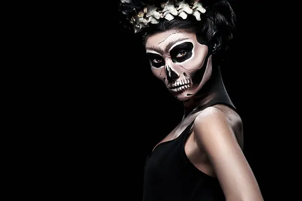 Woman in Halloween costume of Frida Kahlo on black background. Skeleton or skull makeup.