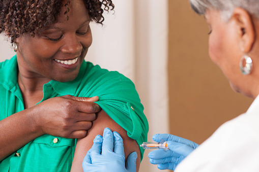 Senior adult doctor or nurse gives flu vaccine to African descent, mid-adult patient at a local medical clinic, hospital, or doctor's office.  NOTE:  This is a studio shot and not an actual medical clinic.