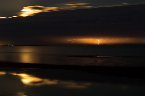 Lightning strikes Moreton Island as a summer storm clears Moreton Bay on the Queensland coastline in the early evening, leaving a rising full moon in its trail. Photographed from Beachmere, Australia, at low tide.