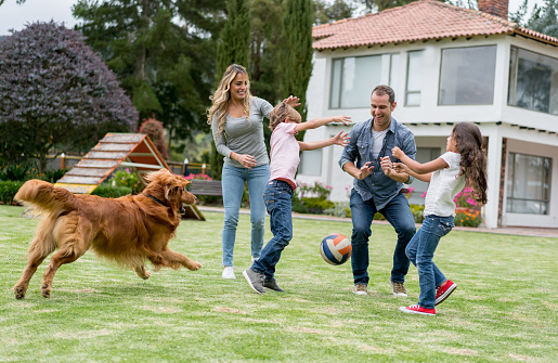 Happy Latin American family playing at the park with a ball and smiling - lifestyle concepts