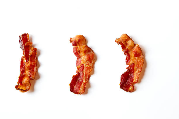 Three Slices of Bacon Isolated on a White Background Three slices of fresh fried bacon lined up in a row isolated on a white background cooked bacon slice stock pictures, royalty-free photos & images