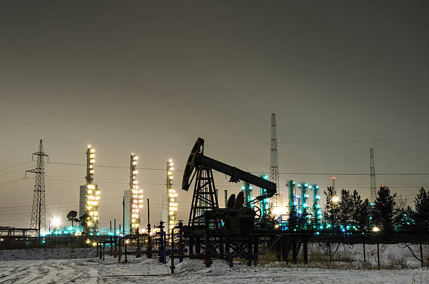 Oil pump and wellhead at the background of refinery Oil pump and wellhead at the background of refinery by night. Oilfield during winter. Oil and gas industry. wellhead stock pictures, royalty-free photos & images