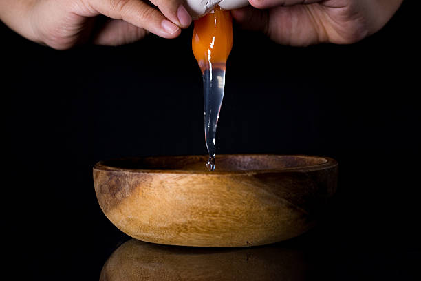 istock Close-up of hands cracking egg and wood bowl on Black 618650274