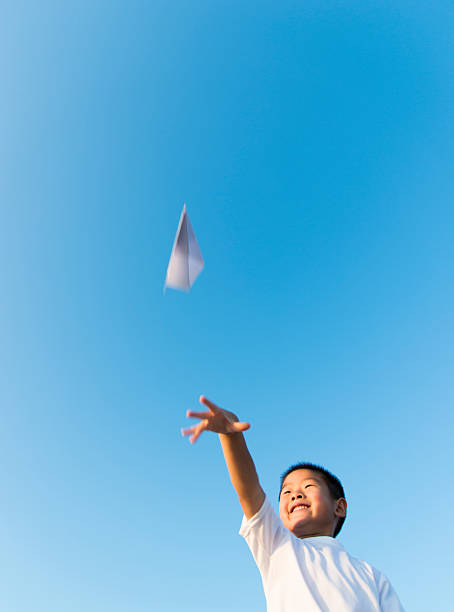 Boy hand holding a paper plane with the view of sky