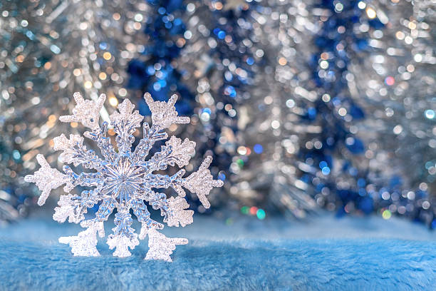 Translucent Christmas toy snowflake on silver-blue bokeh background.