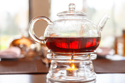 Black tea in glass Cup and glass teapot with a candle stands on the table. A cozy evening at home in the cold season.