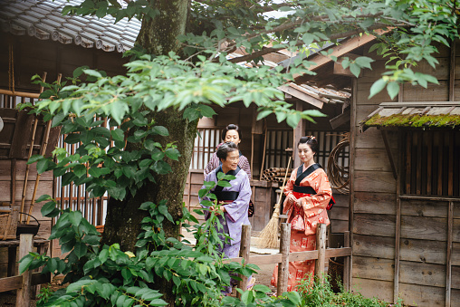 Two young and one elderly Japanese women wearing kimonos and yukatas while walking in traditional Japanese village, followed by Japanese peasants. Image taken with Nikon D800 and developed from RAW in XXXL size, in TOEI studios in Kyoto, Japan