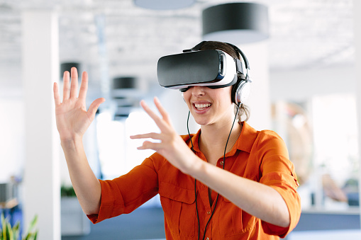 Young woman wearing virtual reality glasses and gesturing in office