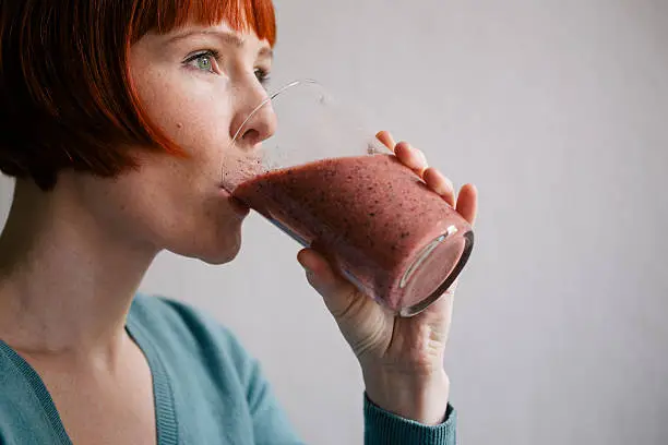 Middle-aged red haired woman enjoying a healthy smoothie with fresh fruits and berries while relaxing at home