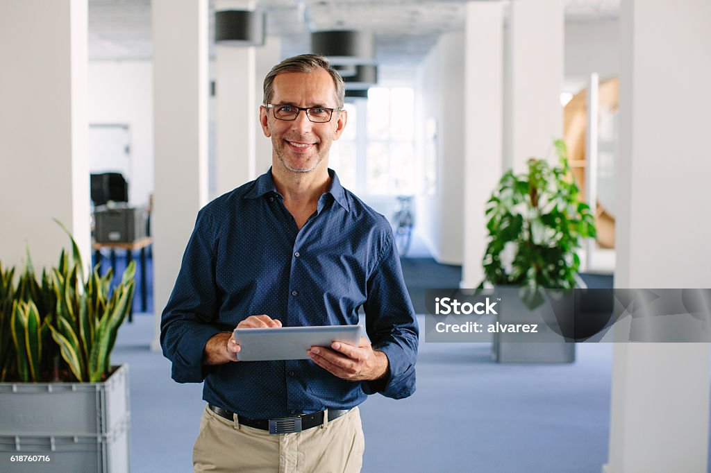 Successful senior businessman standing in office Shot of a successful senior businessman standing in office with digital tablet Manager Stock Photo