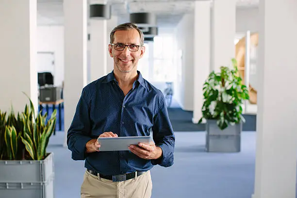 Shot of a successful senior businessman standing in office with digital tablet