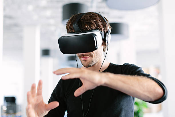Man using virtual reality simulator headset Young man wearing virtual reality glasses and gesturing in office virtual reality stock pictures, royalty-free photos & images