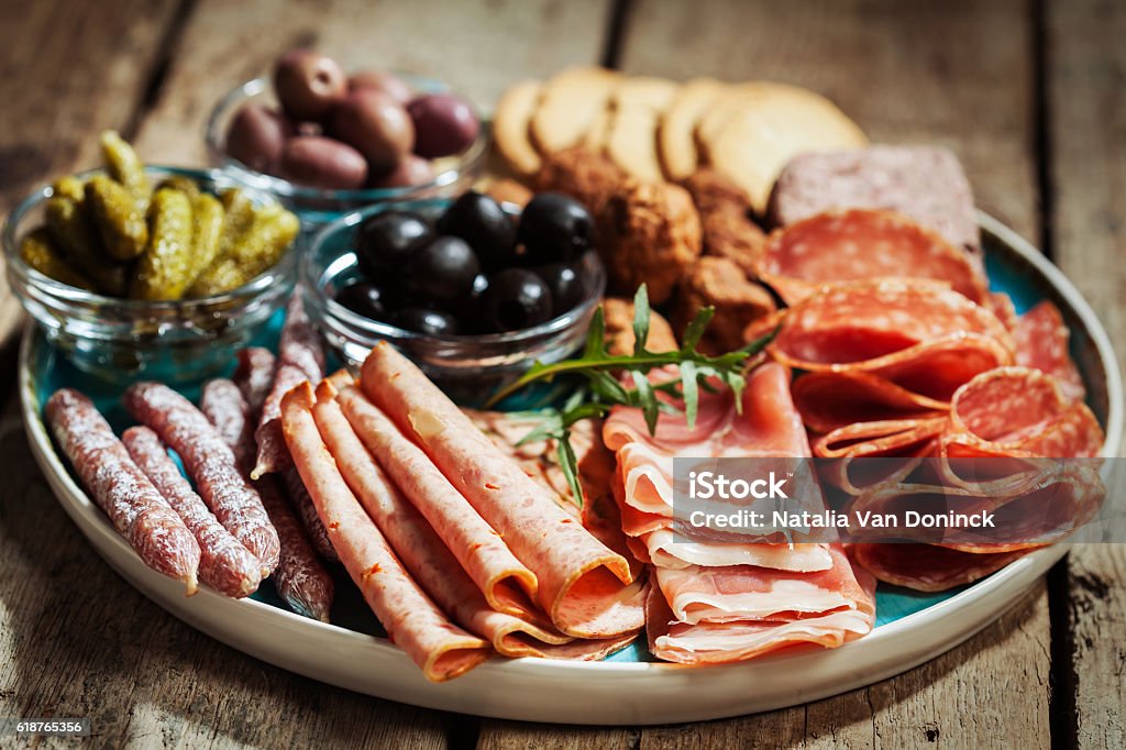 Cold cuts Charcuterie assortment, olives and gherkins  on plate on wooden background Charcuterie Stock Photo