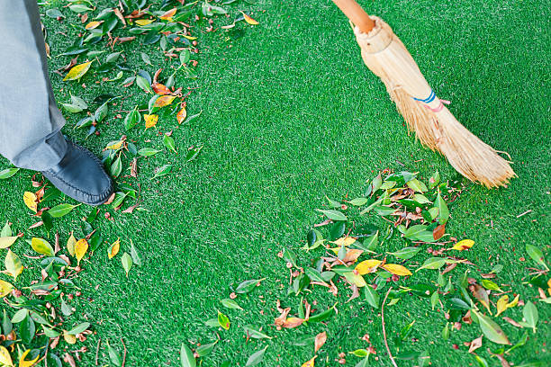 Working with a broom sweeps the lawn from the fallen leaves. The autumn season, working in the yard outdoors.