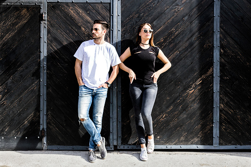 Stylish teenage couple in jean clothes and sun glasses posing on vintage wooden door background