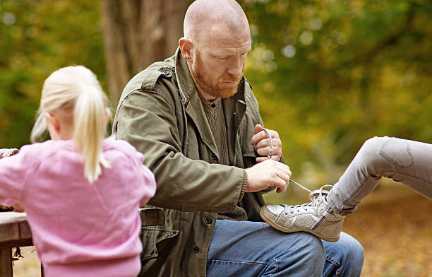Single father tying blonde daughter's shoelace in autumnal surroundings Single father tying blonde daughter's shoelace in autumnal surroundings divorcee stock pictures, royalty-free photos & images