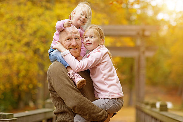 istock Single father and daughters posing together in autumnal park surroundings 618846024