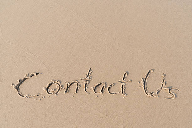 "Contact Us" message written on sand beach stock photo