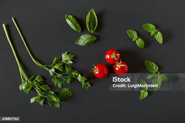 Green Vegetables Around Three Red Tomatoes Stock Photo - Download Image Now - Black Background, Basil, Parsley