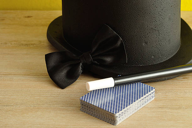 A magicians hat displayed with a wand, bow tie and a deck of cards