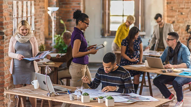 Busy coworking space Large group of people in a large room with desks and computers, looks like a start up or coworking space. busy stock pictures, royalty-free photos & images