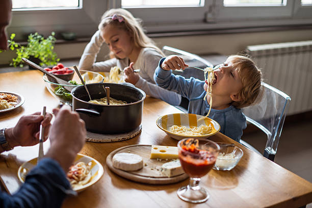 Enjoying great lunch Happy family enjoying lunch while kids playing. kids eating noodles stock pictures, royalty-free photos & images