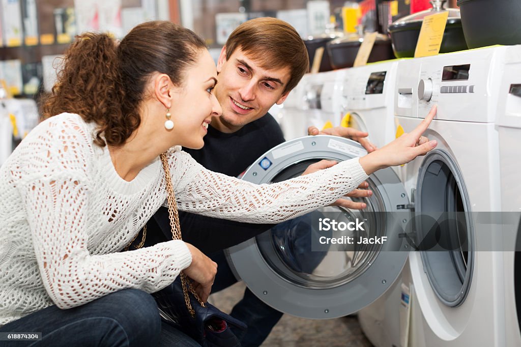Young couple choosing washing machine in hypermarket and smiling Young couple choosing washing machine in supermarket and smiling Shopping Stock Photo