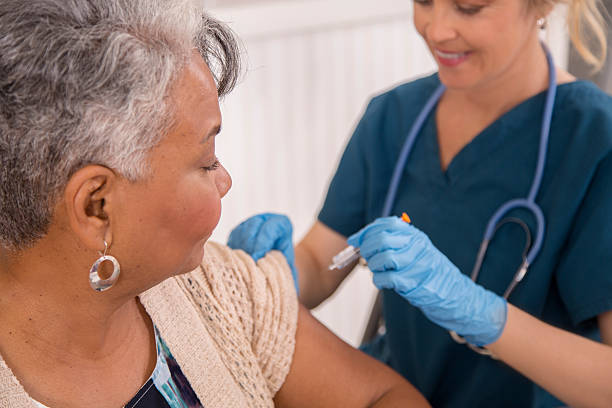 Nurse gives flu vaccine to senior adult patient at clinic. stock photo